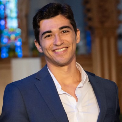 Young man with dark hair and smiling wearing white shirt and navy jacket in church